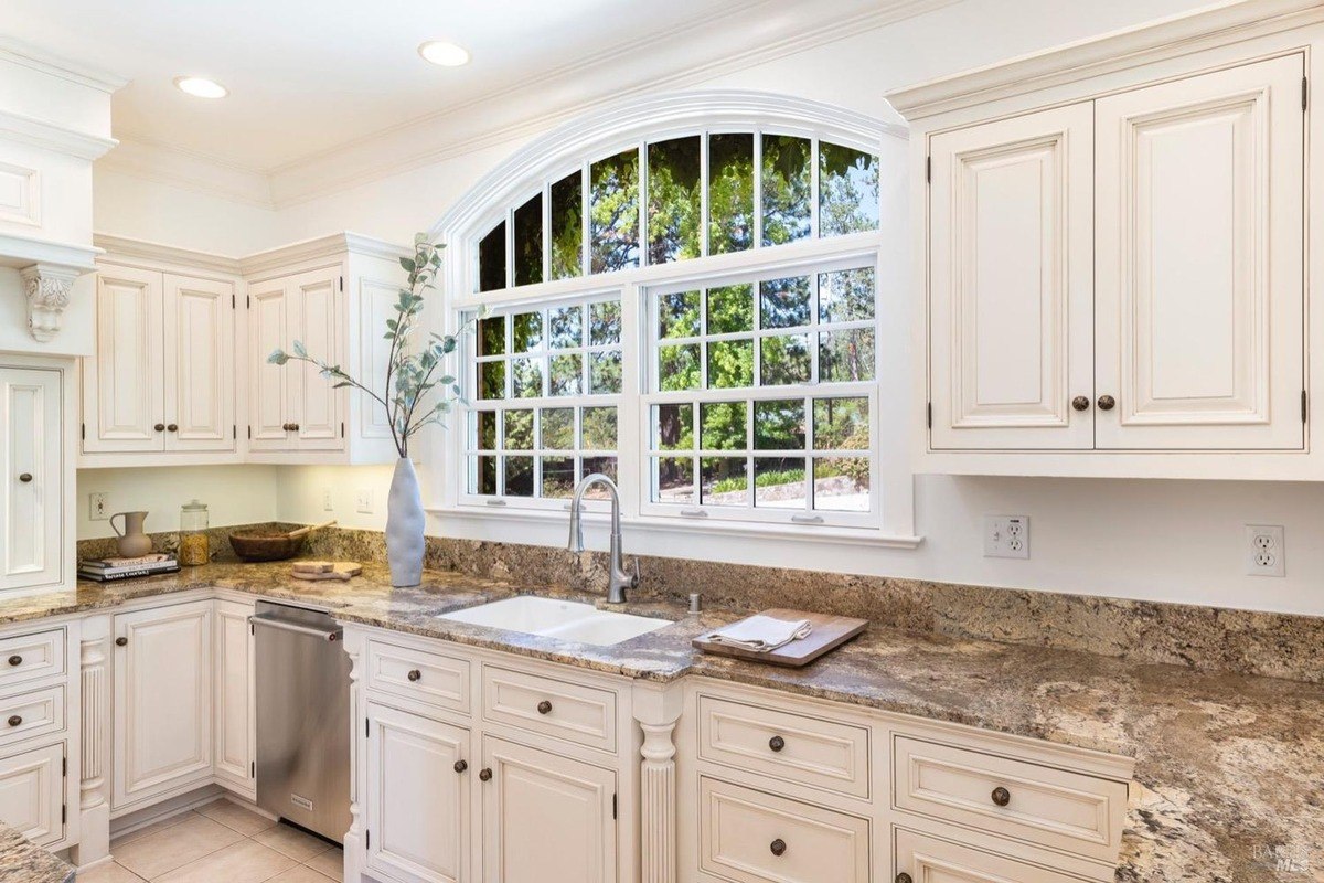 White cabinets, granite countertops, and a large arched window overlooking trees.