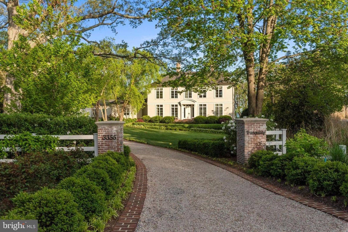 Long driveway leads to a large, two-story house, surrounded by lush landscaping and trees.