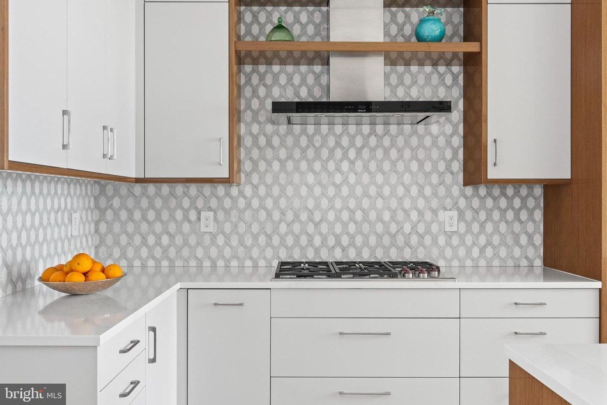 Modern kitchen features white cabinets, gray patterned backsplash, and a gas cooktop.