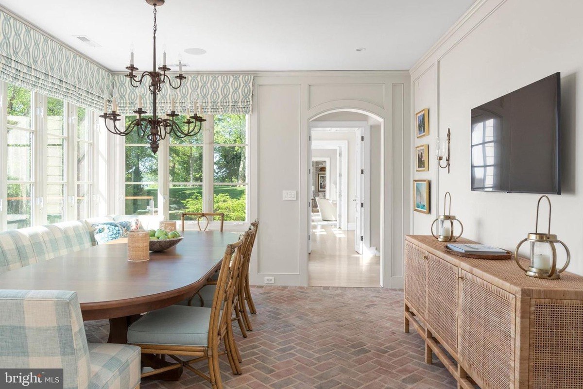 Dining area features a large wood table, light blue cushioned chairs, and a brick floor.