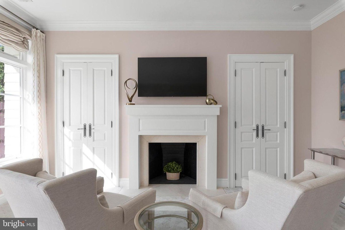 Relaxing sitting area features blush-colored walls, a white fireplace, and comfortable armchairs.