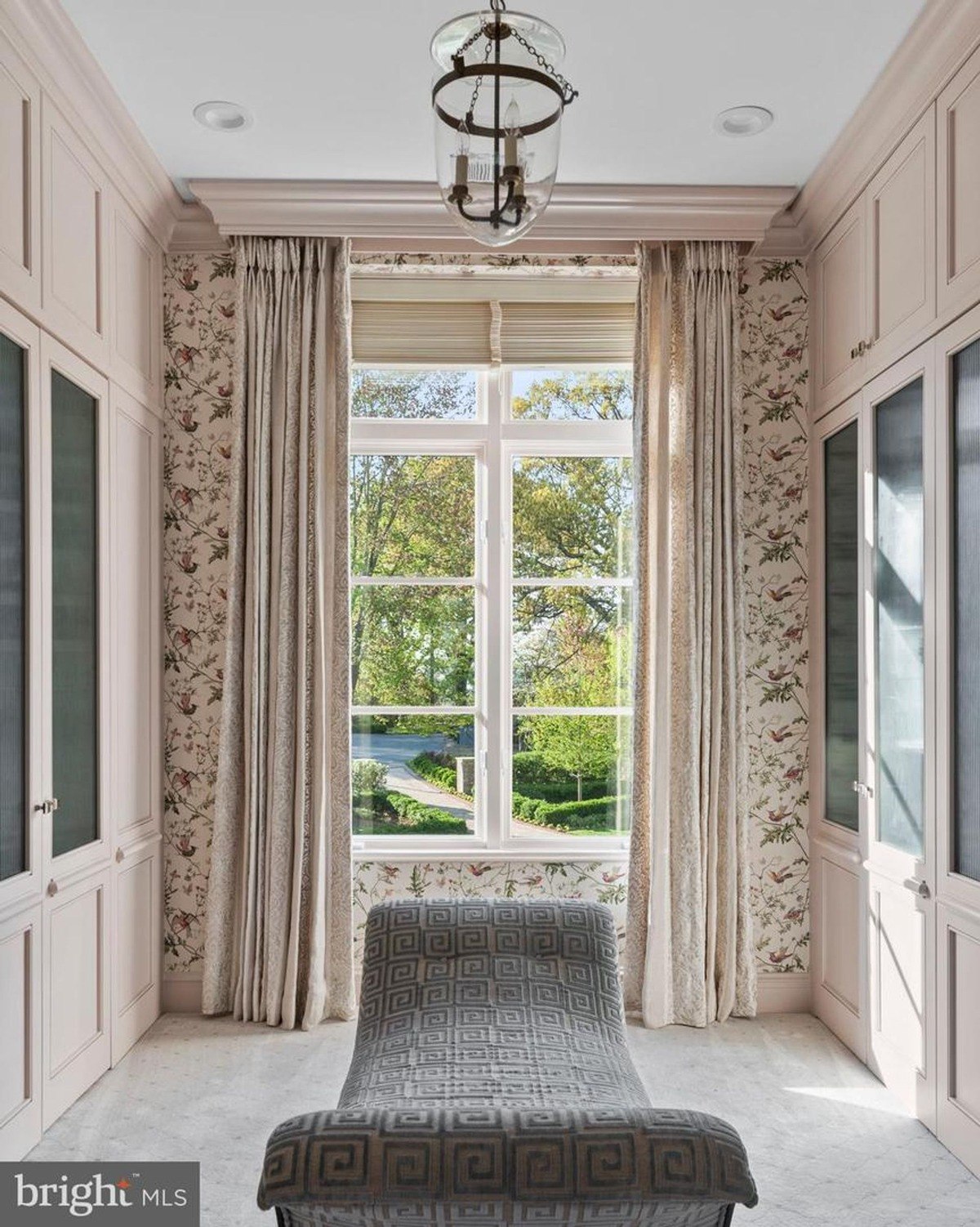 Relaxing room features floral wallpaper, a chaise lounge, and a window with a view of a garden.