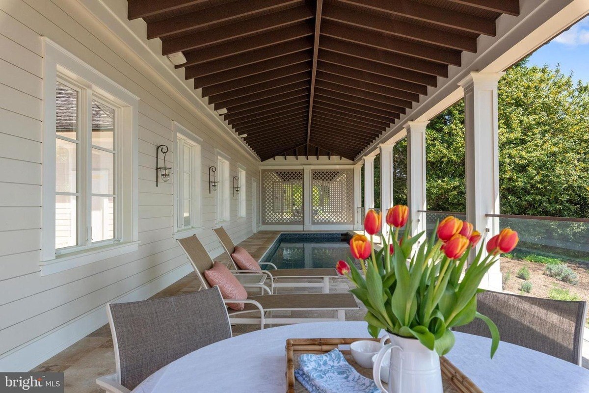 Covered patio overlooks a pool, featuring lounge chairs and a table with tulips.