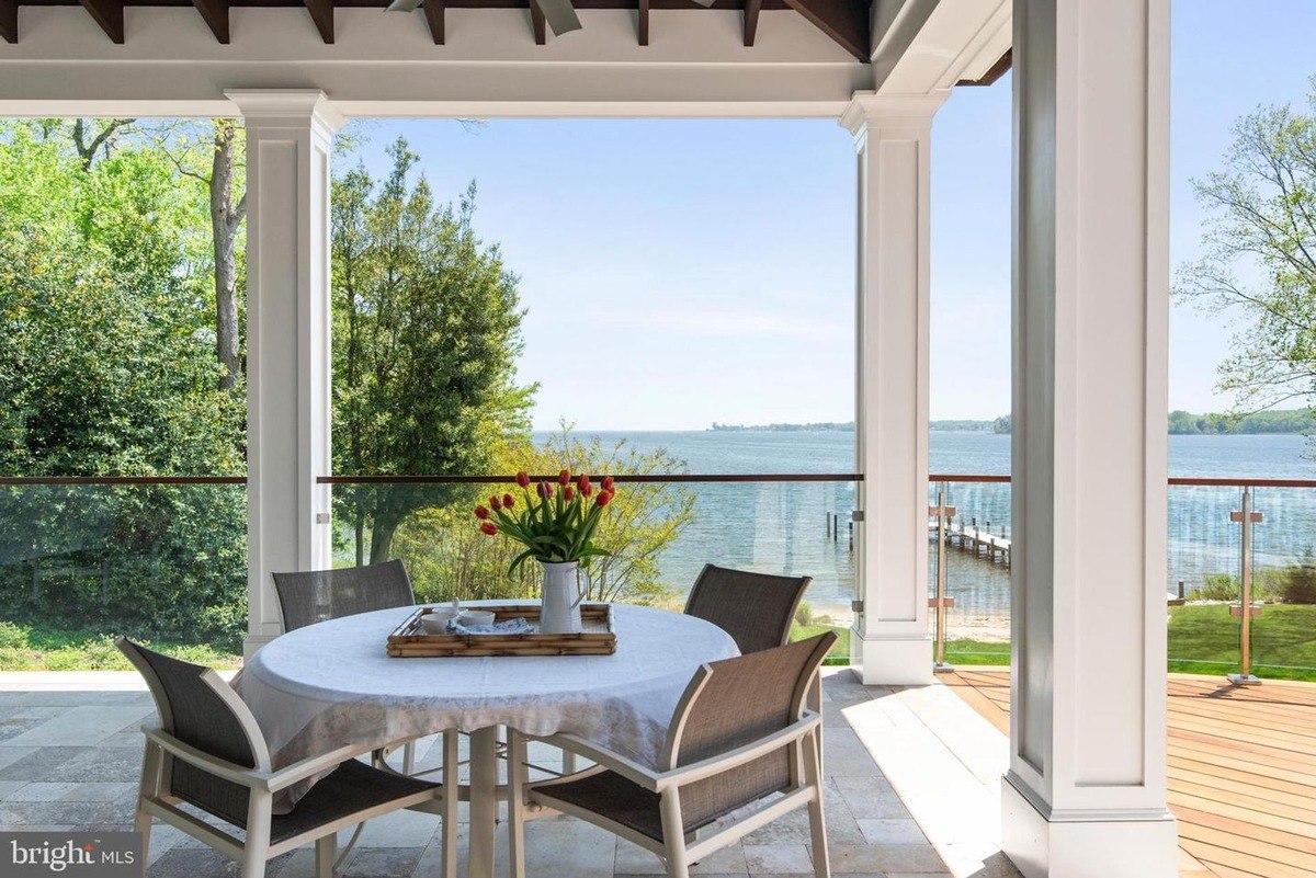 Outdoor dining area with water views, featuring a table, chairs, and a glass railing.