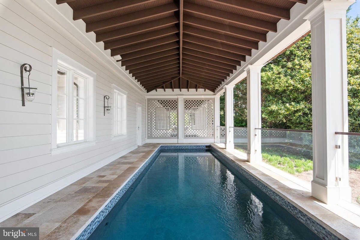 Lap pool is situated under a covered structure with wood beams and light-colored siding.