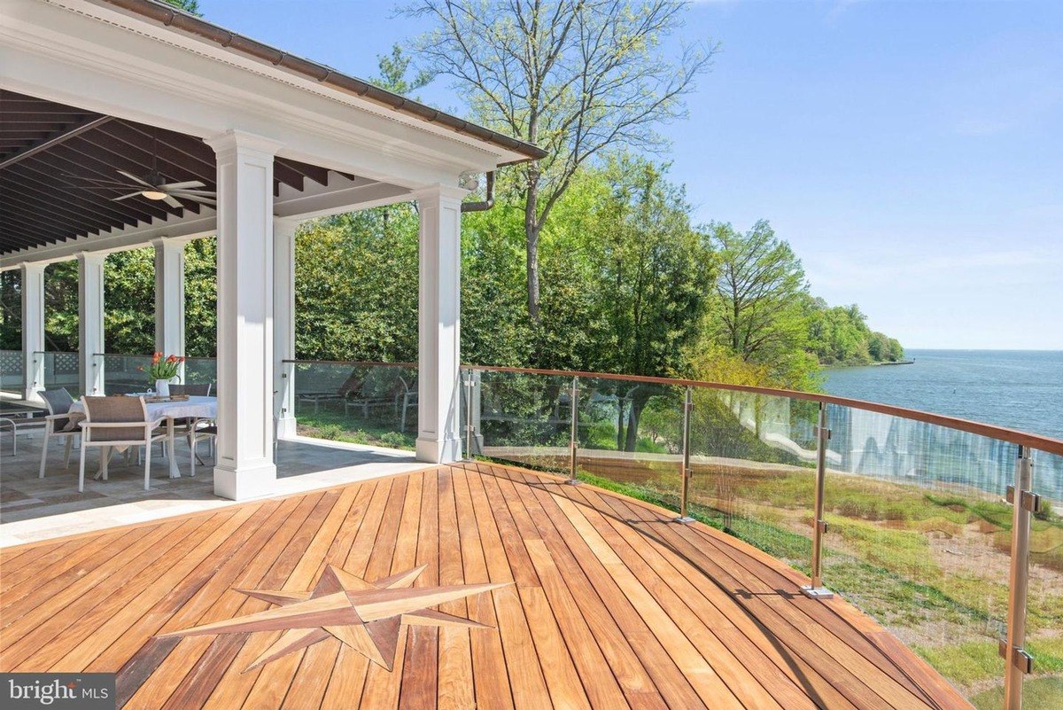 Expansive deck overlooks a waterfront, featuring a dining area and a glass railing.