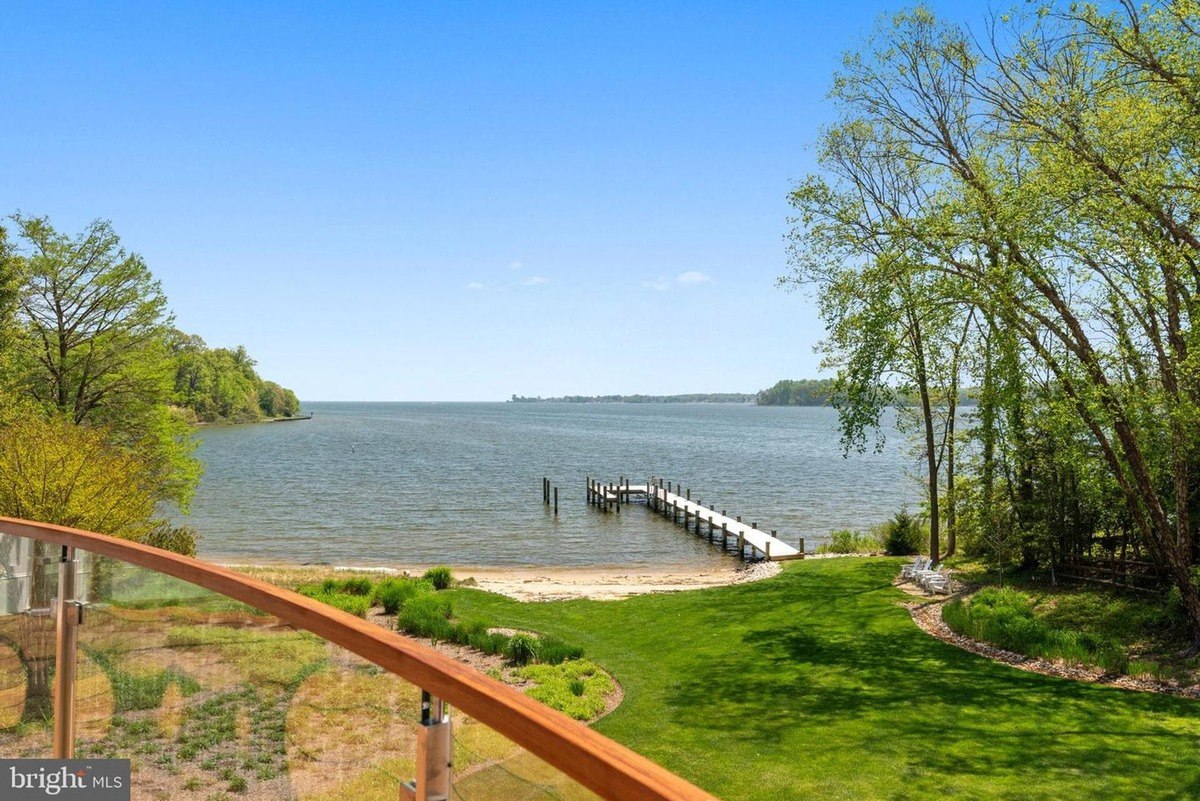 Waterfront property features a grassy yard leading to a private dock and calm waters.