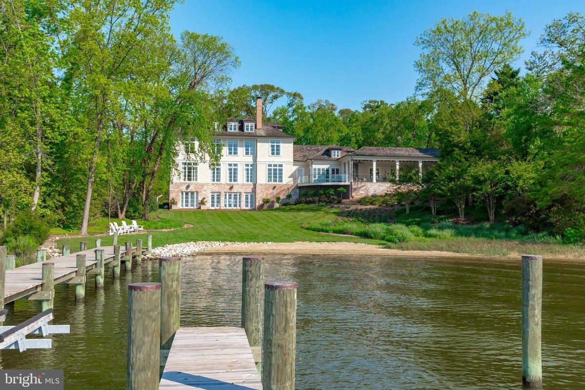 Large waterfront home sits on a grassy lot with a private dock extending into the water.