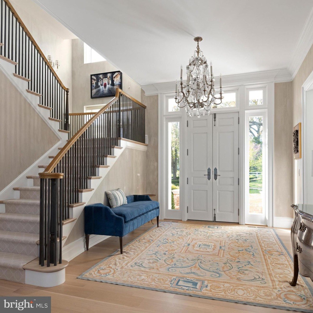 Grand foyer features a sweeping staircase, ornate chandelier, and patterned area rug.