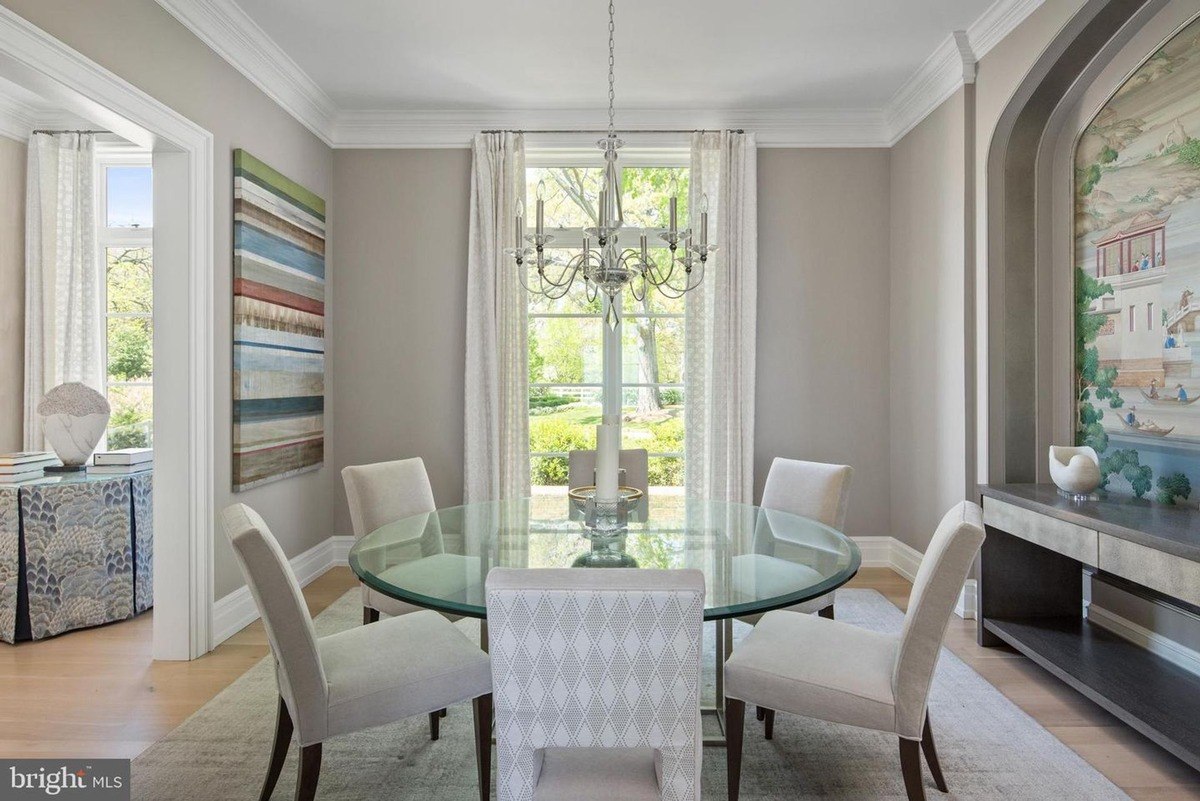 Formal dining room features a glass-top table, neutral-toned chairs, and a large window overlooking a garden.