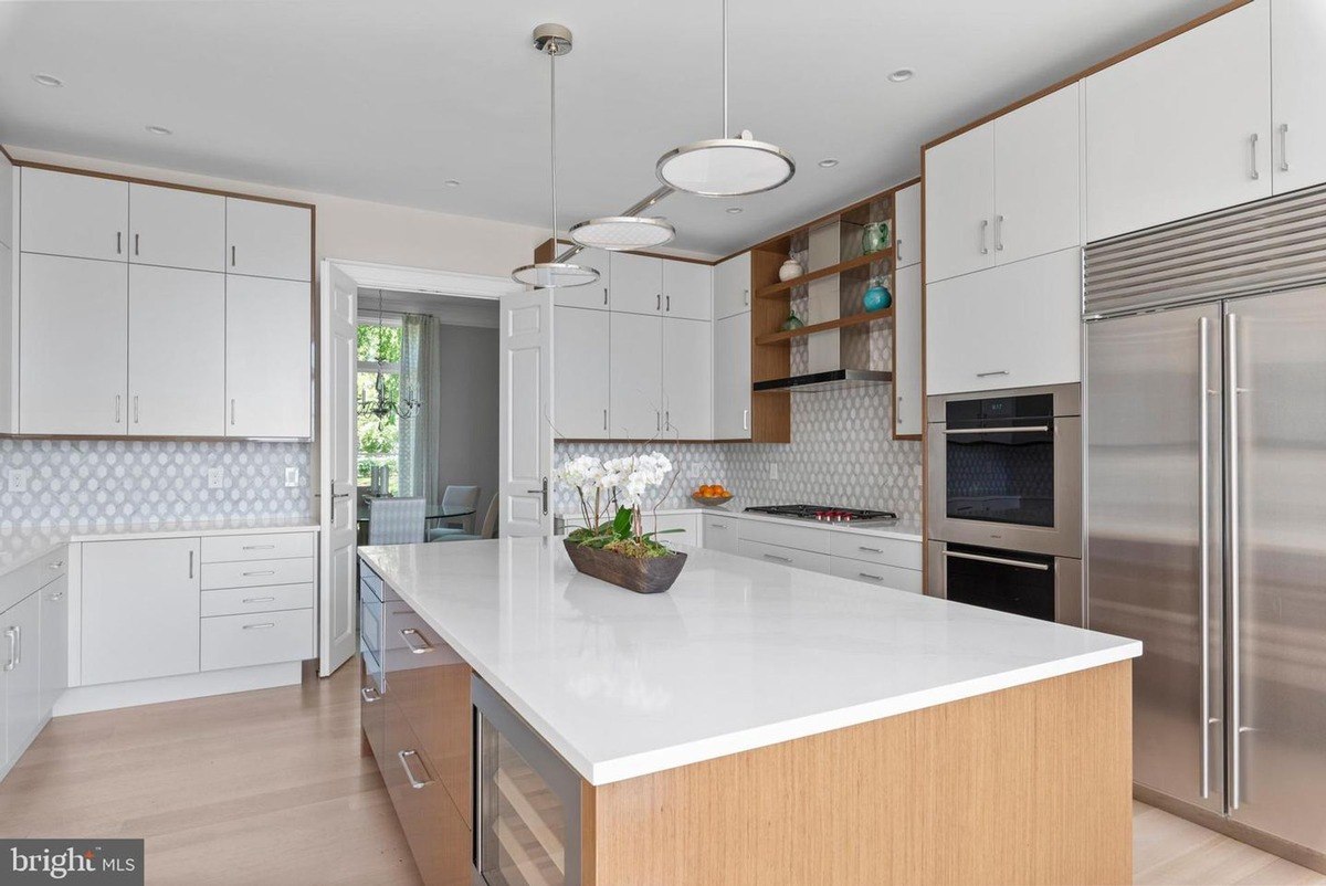 Modern kitchen features white cabinets, stainless steel appliances, and a large island with a white countertop.