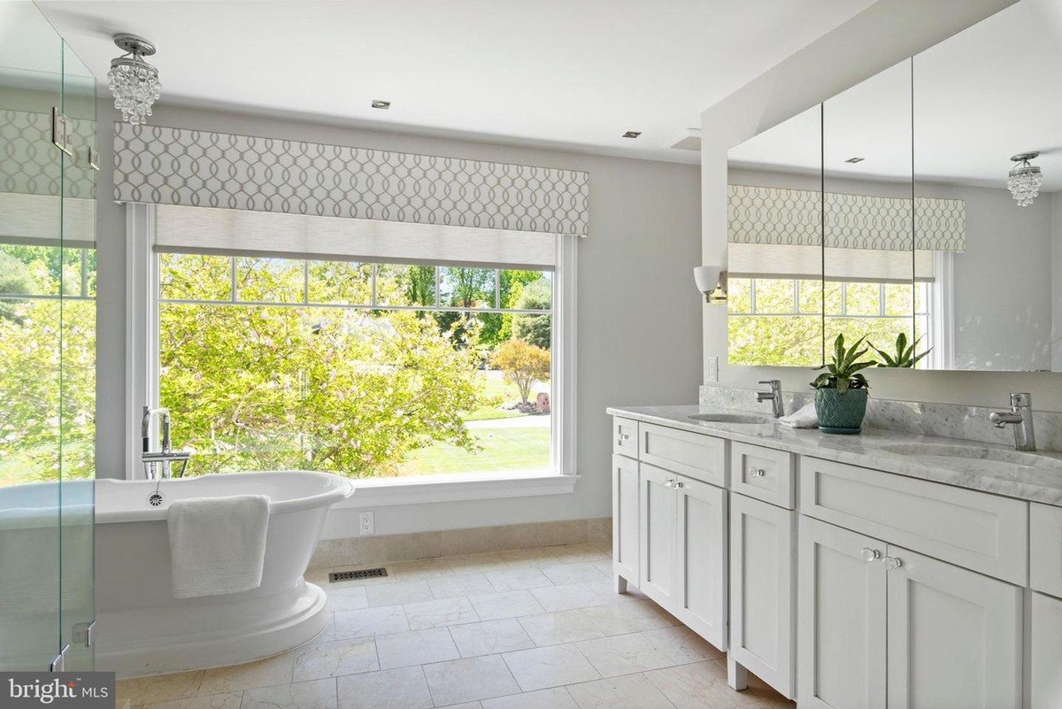 Bathroom has a large soaking tub, double vanity, and a view of trees.