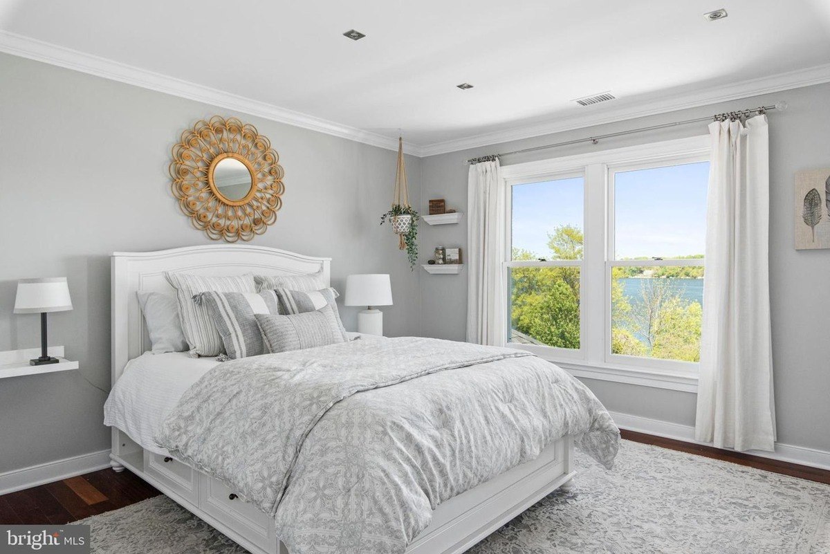 Bedroom has a white bed, large window with a water view, and gray walls.