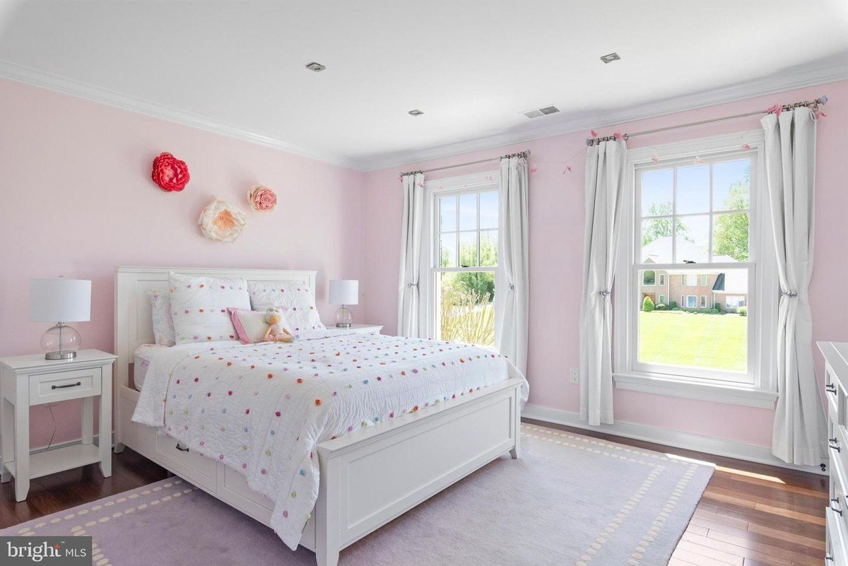 Bedroom has a white bed, pink walls, and a view of a yard.