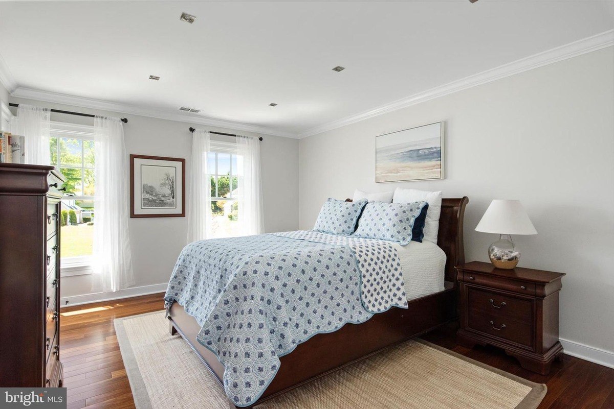 Bedroom has a bed with a blue and white quilt, hardwood floors, and a view of a yard.