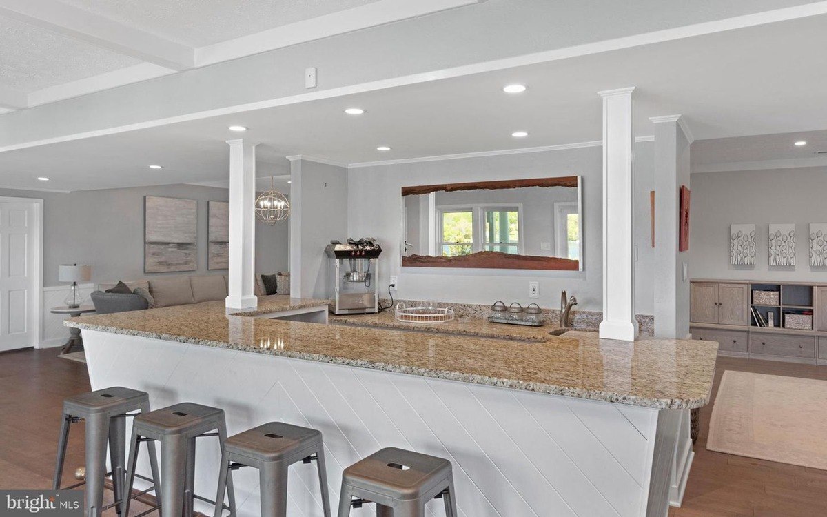 Basement bar has granite countertops, white cabinets, and bar stools.