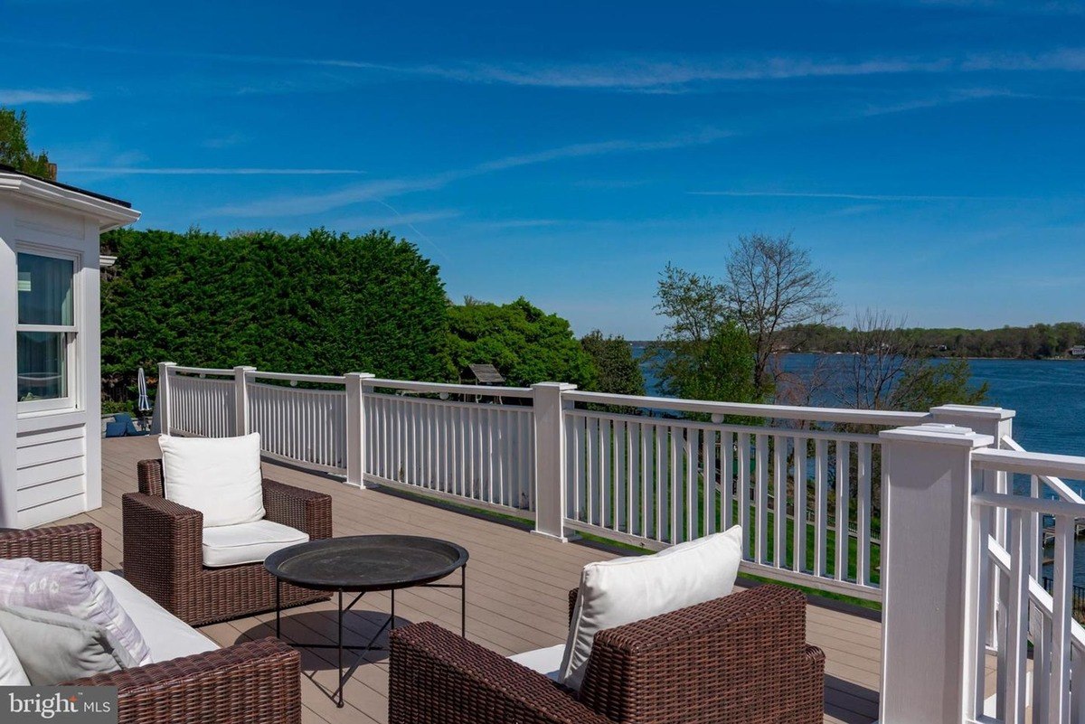 Deck has wicker furniture, white railing, and a water view.