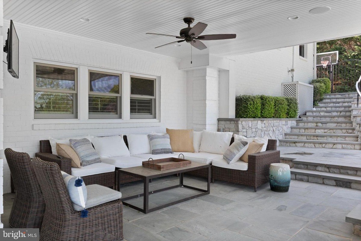 Patio has wicker furniture, ceiling fan, and stone steps.