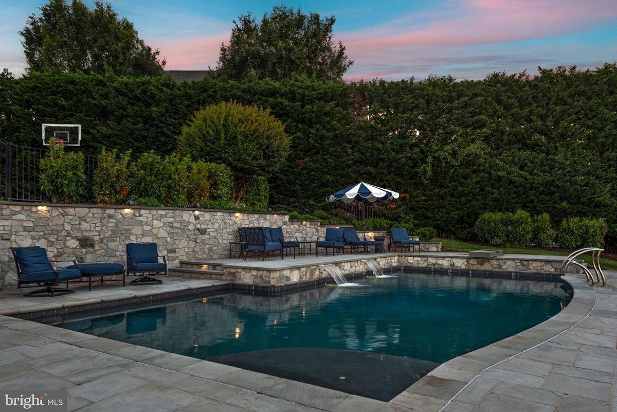 Pool area has a swimming pool, stone walls, and patio furniture.