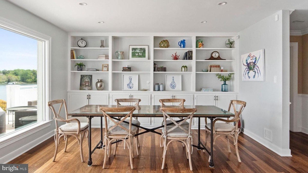 Dining room has a large built-in shelving unit, a wood table, and a view of water.