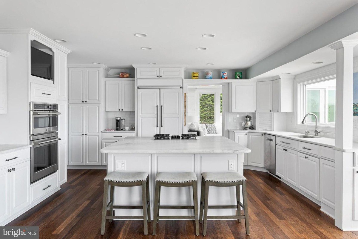 Kitchen has white cabinets, a large island, and hardwood floors.