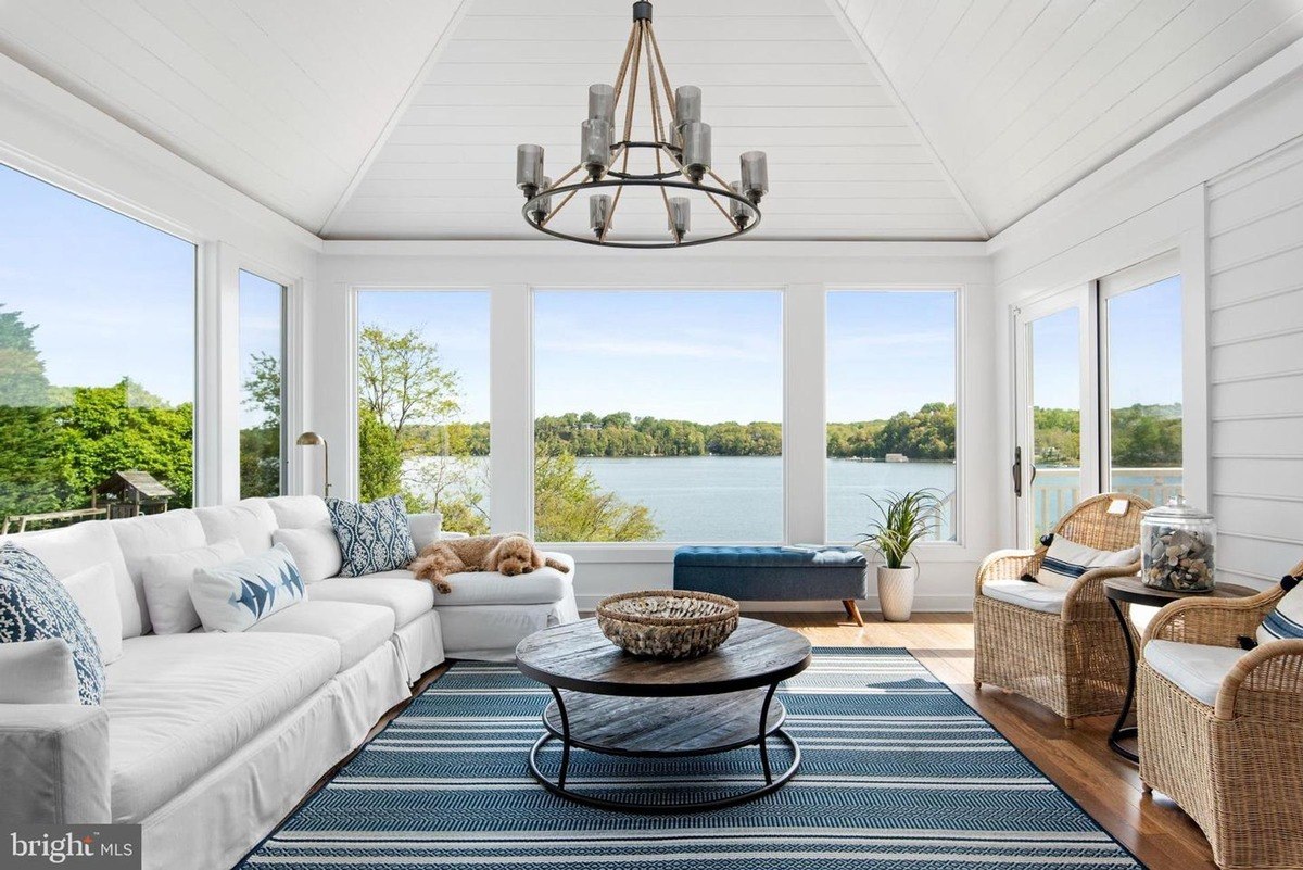 Room has a white couch, wicker chairs, and a view of a lake.