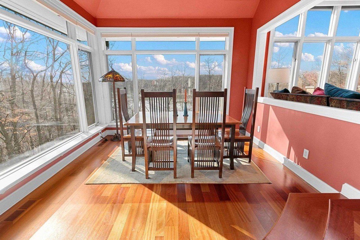 Dining room has hardwood floors, orange walls, large windows with a view, and wooden dining set.