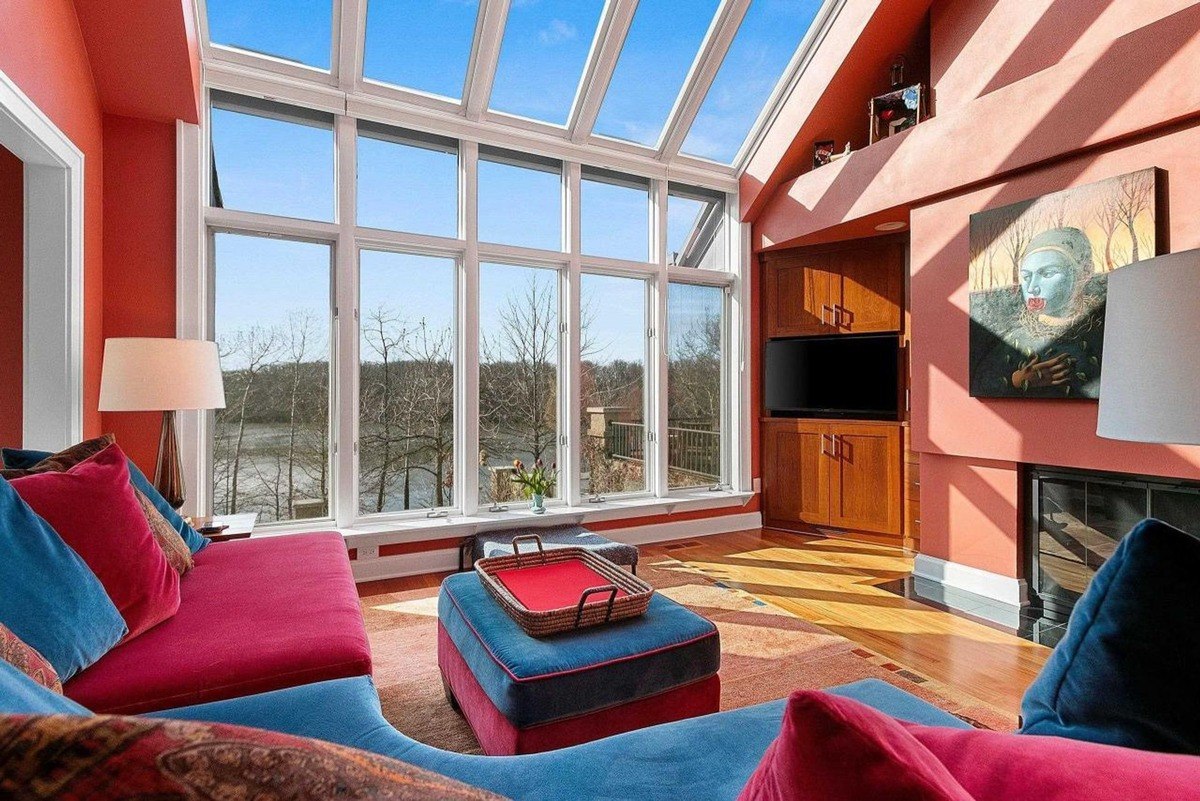 Room with orange walls, large windows with a view, sectional sofa, and hardwood floors.