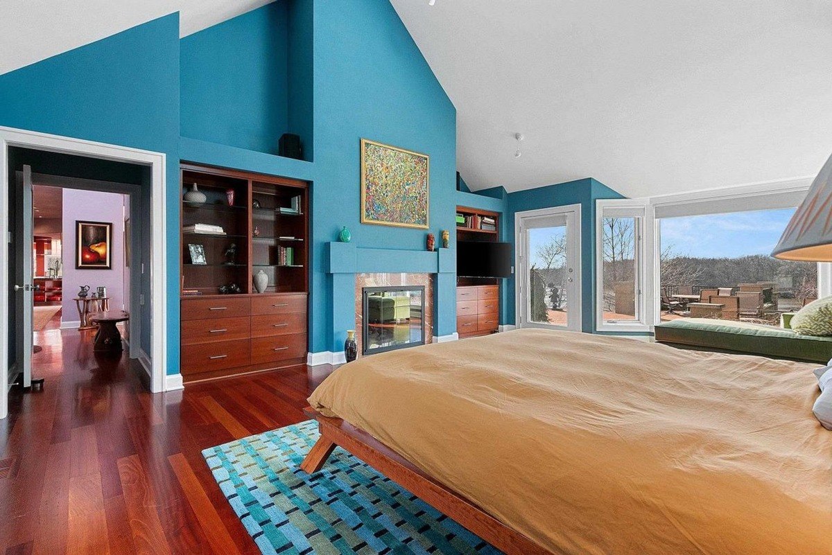  Hardwood floors and large windows with a view create a bright and airy atmosphere in this bedroom, accented by blue walls and a comfortable bed.