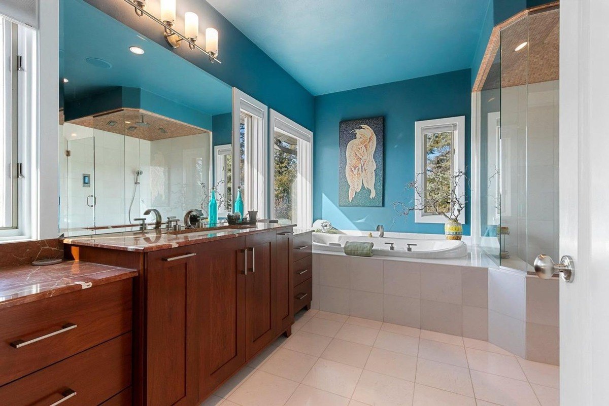 Bathroom has blue walls, wood cabinets, marble countertops, and a large bathtub.