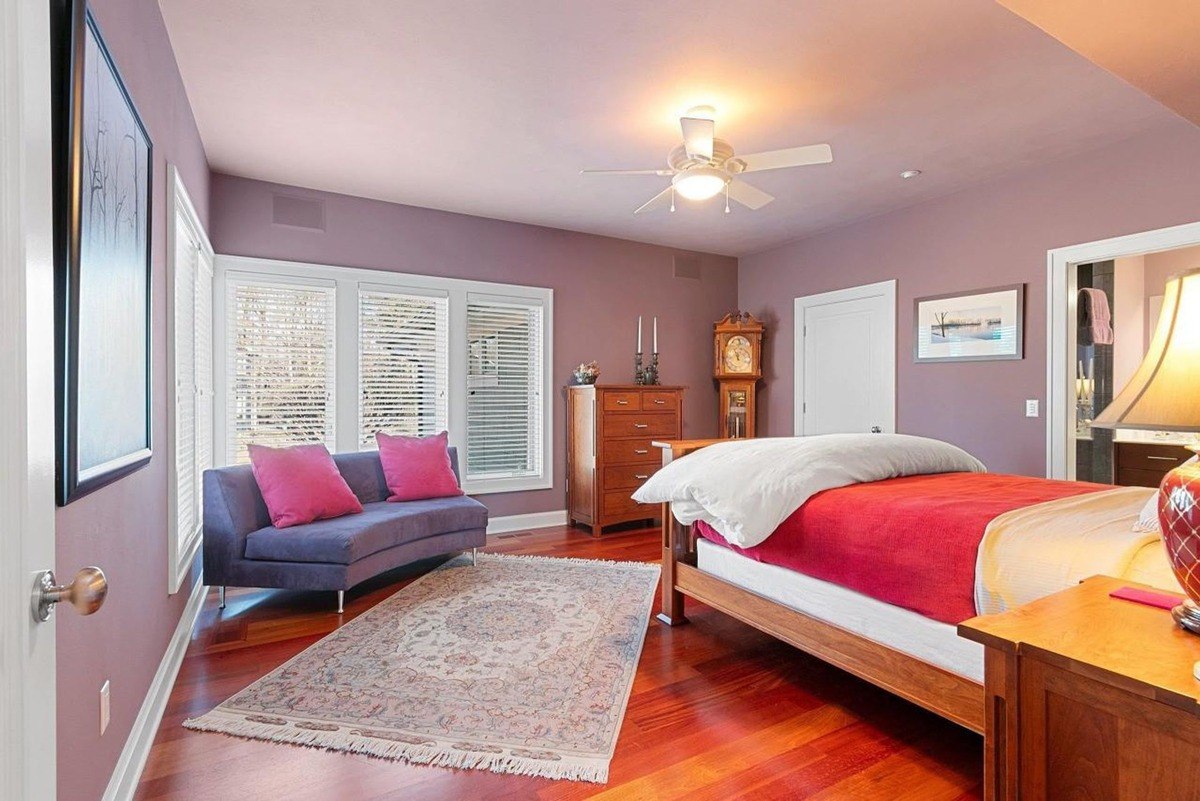 Bedroom has hardwood floors, purple walls, a bed with red bedding, and a seating area.