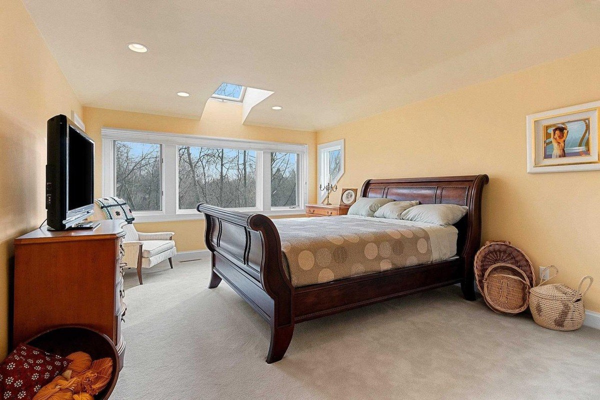 Bedroom, with its beige walls and carpeted floor, includes a sleigh bed with patterned bedding and large windows offering a view.