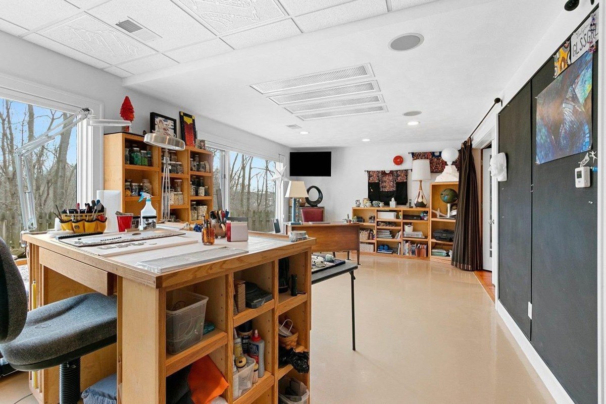 Room with large windows, wood work table, shelves, and a large black board.