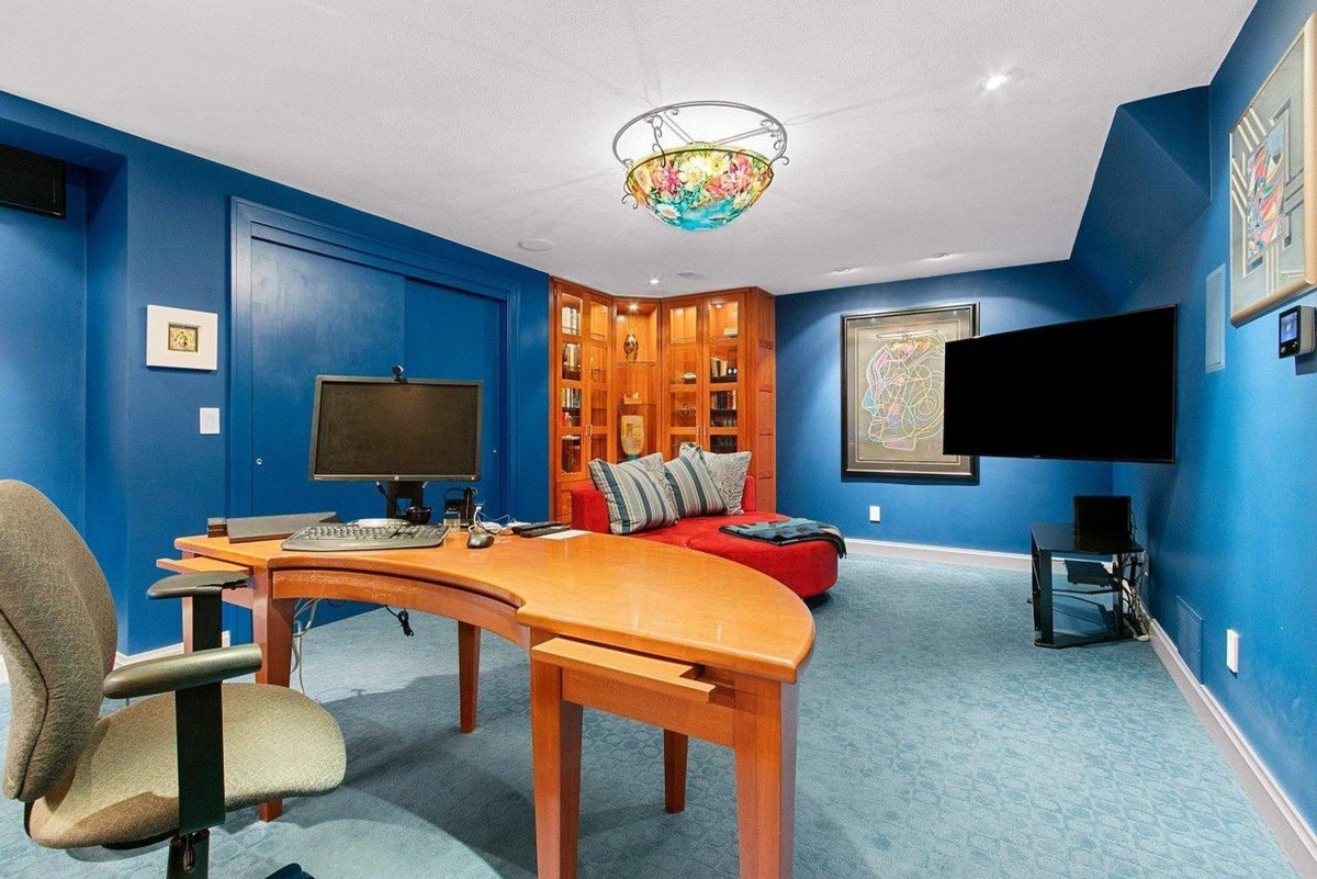 Room has blue walls, wood desk, computer, and a large flat screen TV.