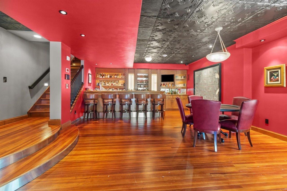 Room has red walls, wood floors, a bar, and a poker table with chairs.