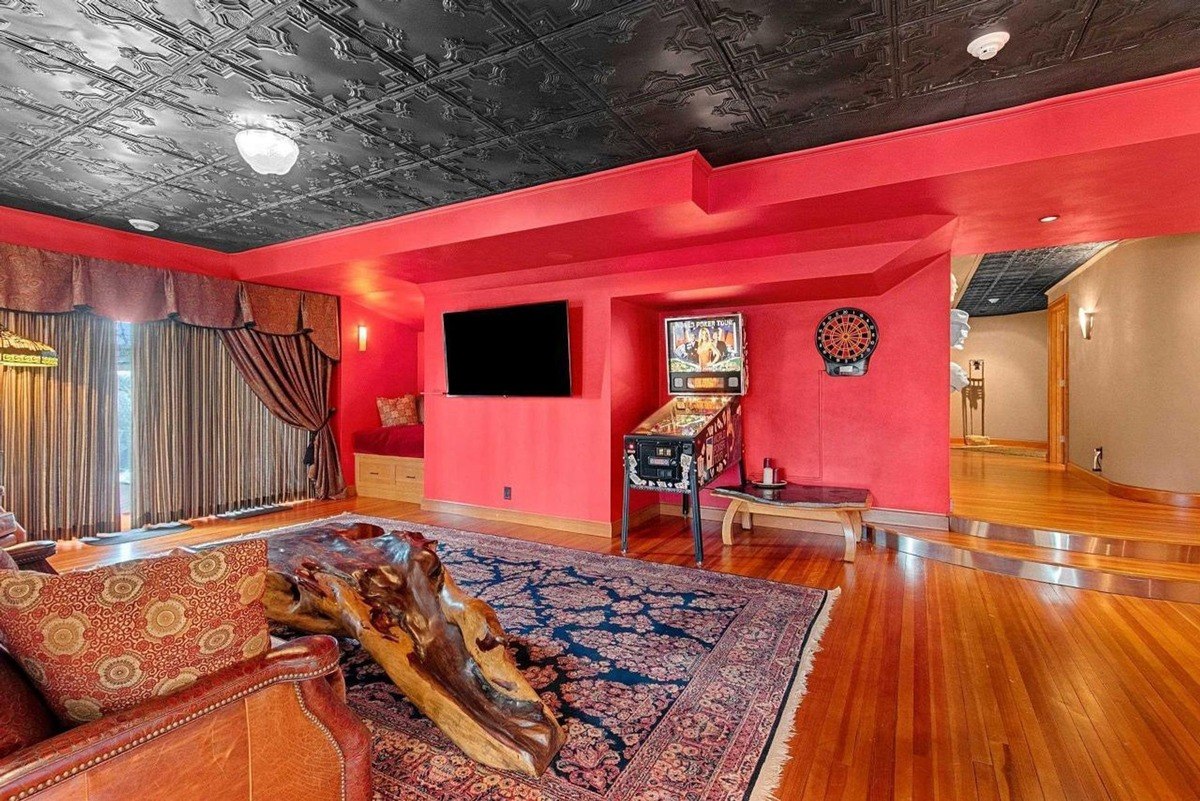 Room has red walls, wood floors, a wood slab coffee table, and a pinball machine.