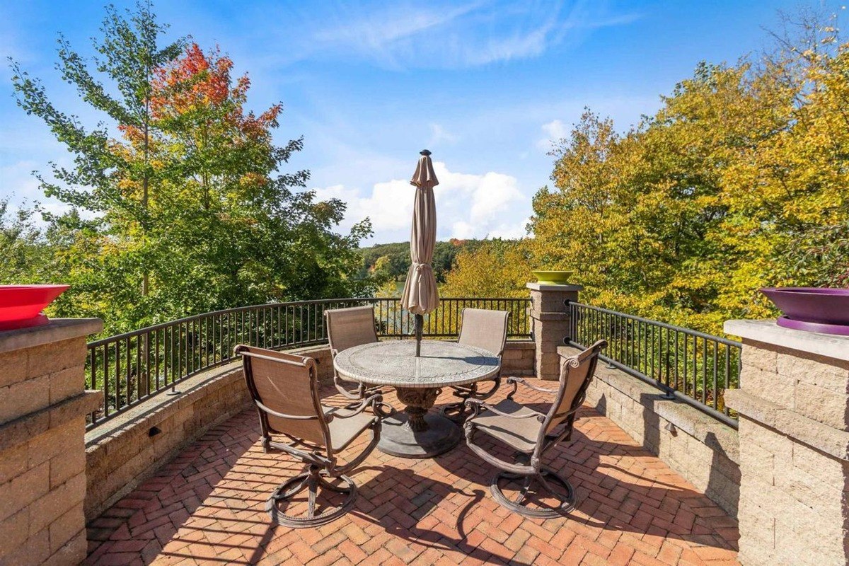 Patio has brick flooring, a round table with chairs, and a view of trees.