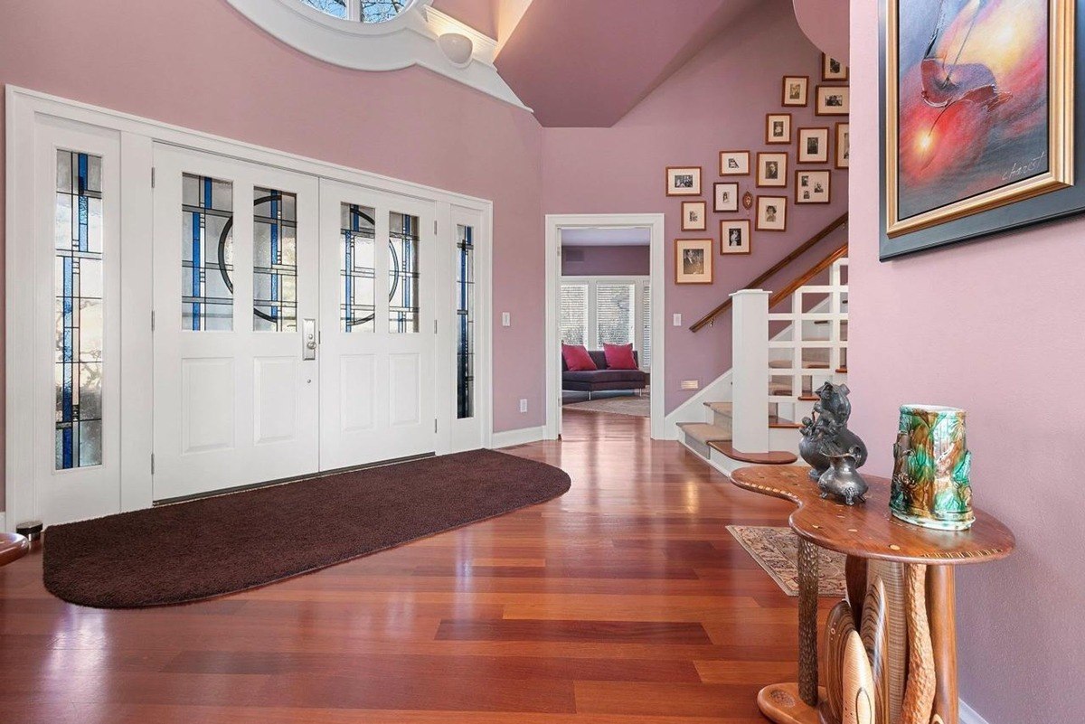 Home with hardwood floors, pink walls, double doors with stained glass, and a staircase with framed photos.