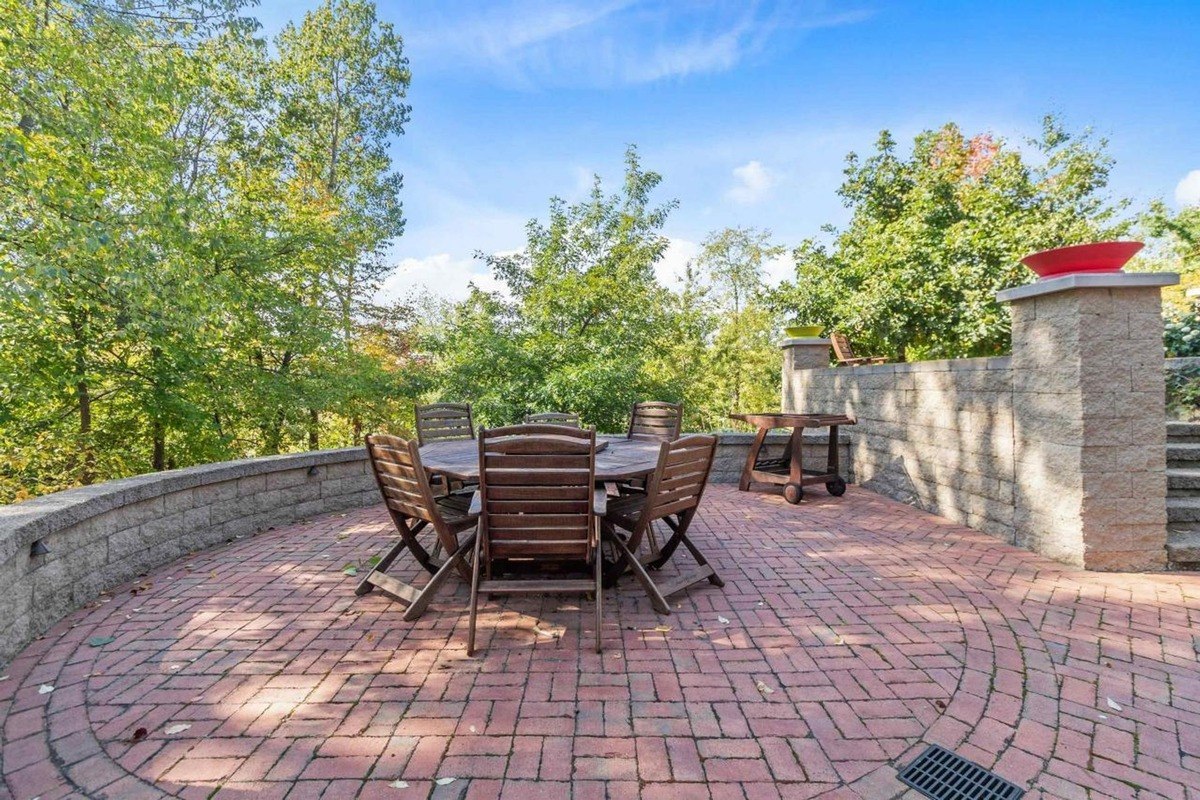 Patio with brick flooring, a round table with chairs, and a view of trees.