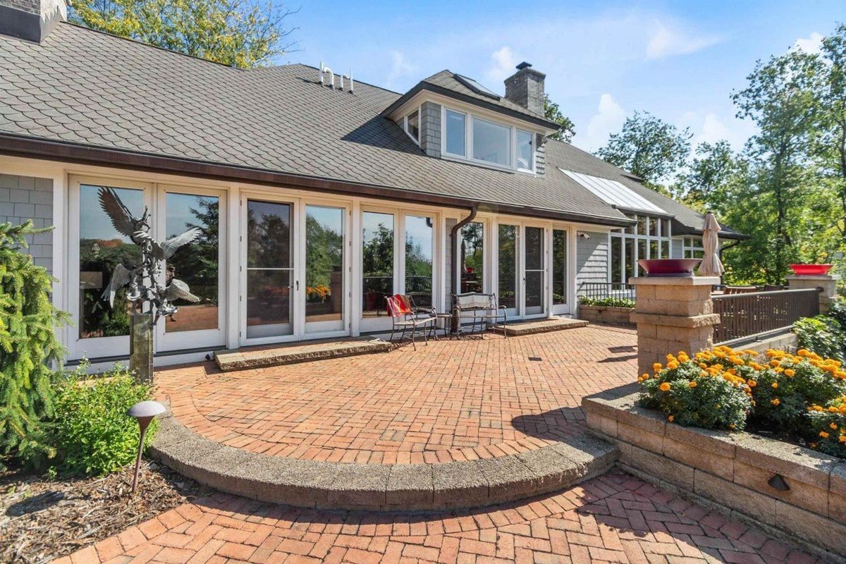 Brick patio is in front of house with large windows and sculpture