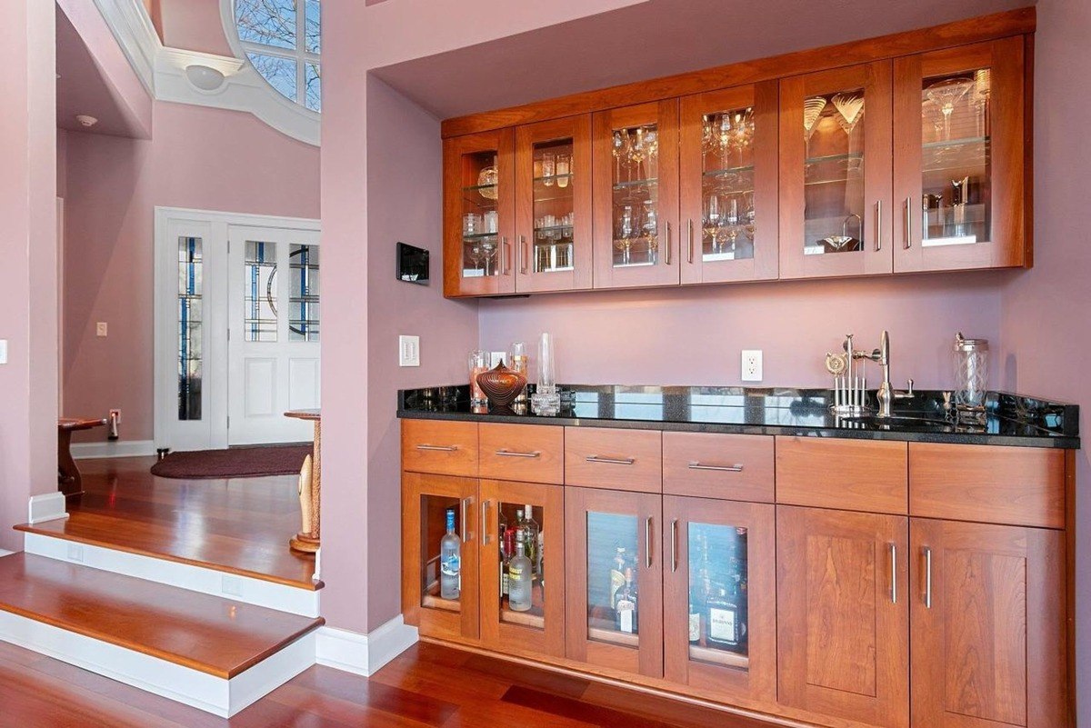 Built-in wooden bar with glass doors and black countertop.