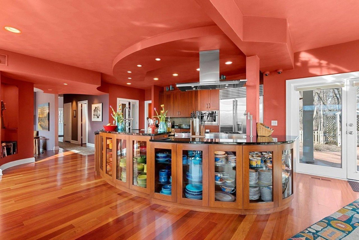 Curved kitchen with glass-front cabinets, hardwood floors, and orange walls.