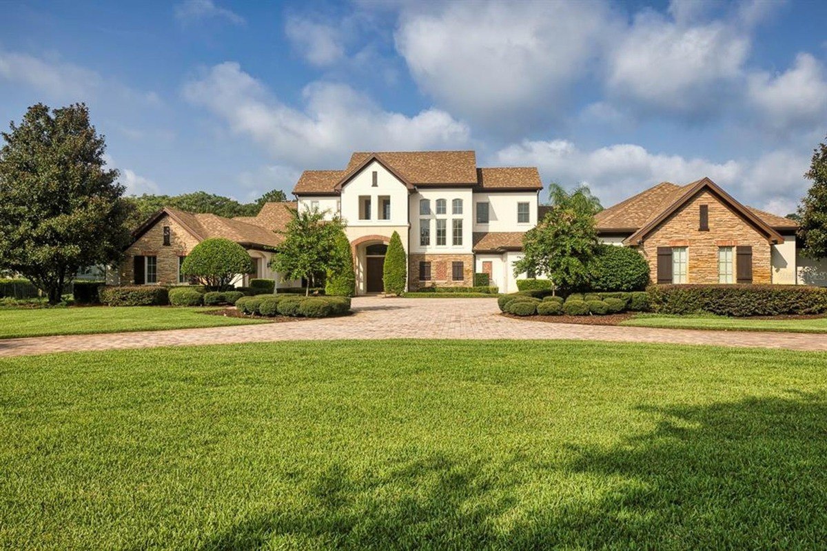 Large house has a brown roof, white siding, and is surrounded by a manicured lawn.