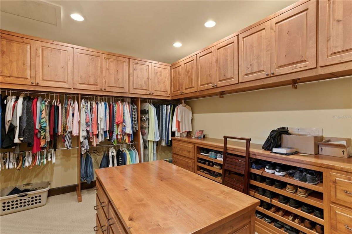 Walk-in closet features extensive shelving, hanging rods, and wooden cabinetry. coldwellbanker-dade-city-fl-jan0425-10