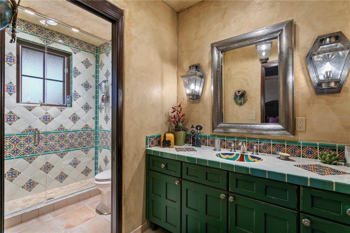 Bathroom features a dark green vanity with a colorful tiled backsplash and a shower with patterned tiles.