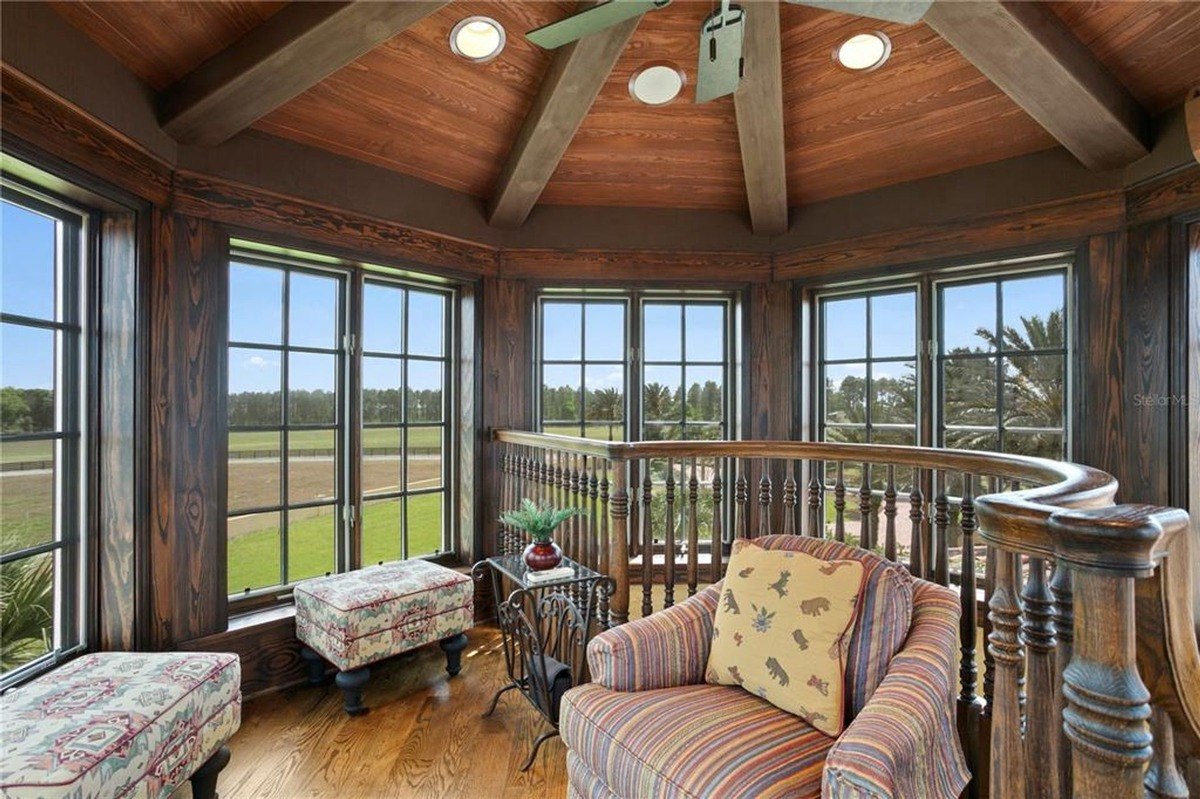 Upper-level room features a curved seating area with large windows offering scenic views and a wood-beamed ceiling.