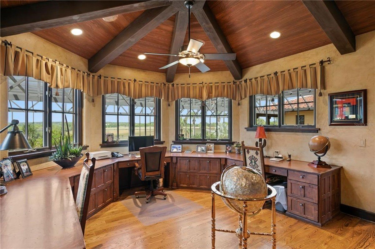 Home office features a built-in desk with a view, a ceiling fan, and wood-beamed ceilings.