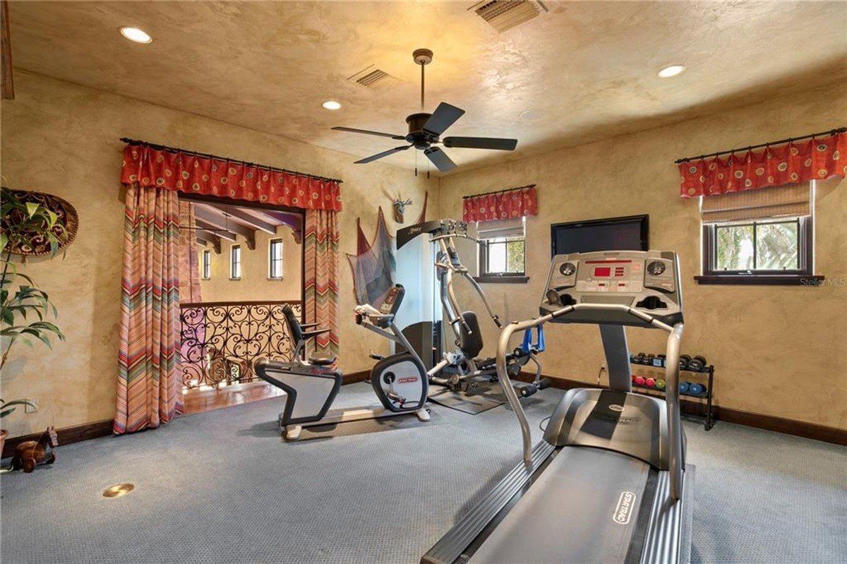 Home gym includes a treadmill, exercise bike, and weight rack, with a view of an upper level balcony.