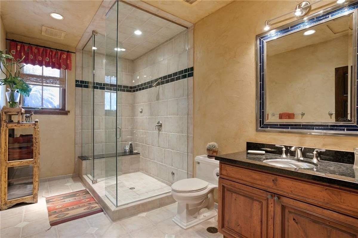 Bathroom features a large glass-enclosed shower, a wooden vanity with a granite countertop, and textured walls.