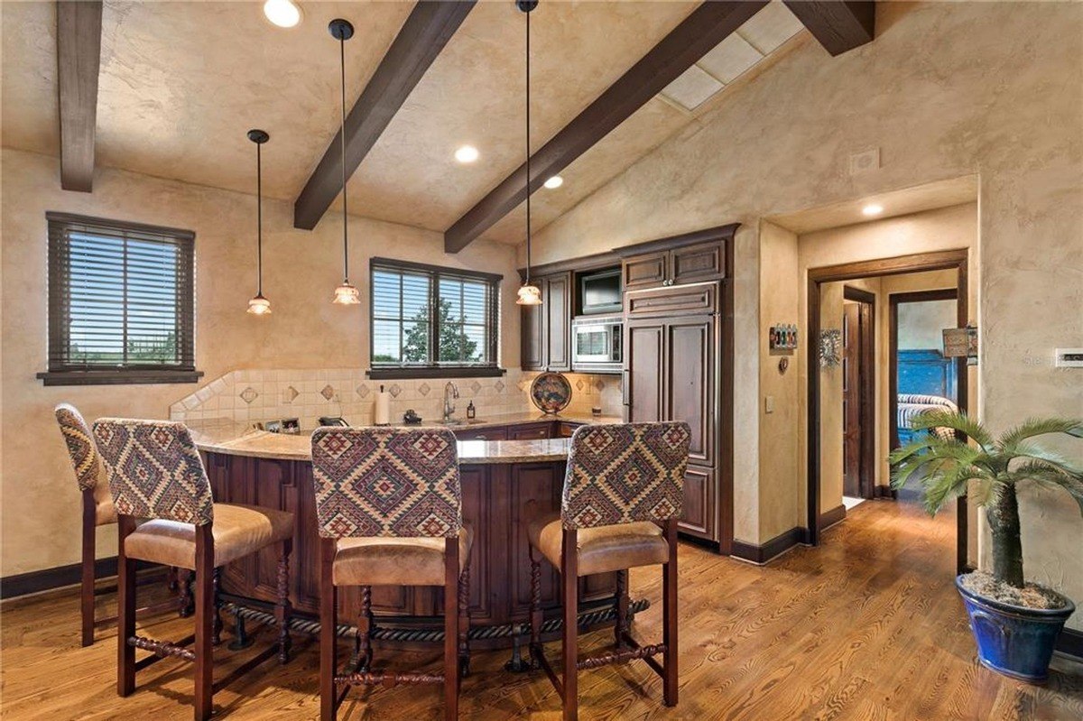 Wet bar area features a curved counter with bar stools, pendant lighting, and wood-beamed ceilings.